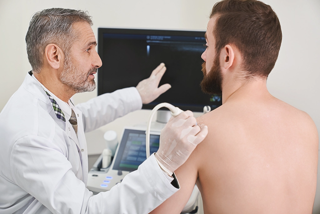Ultrasound Technologist Explaining Images Of Shoulder To Patient