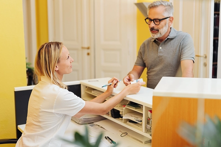 Receptionist Helping Patient Check In For Appointment