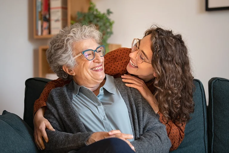 Daughter Smiling At Elderly Mother Experiencing Symptoms Of Alzheimers Disease